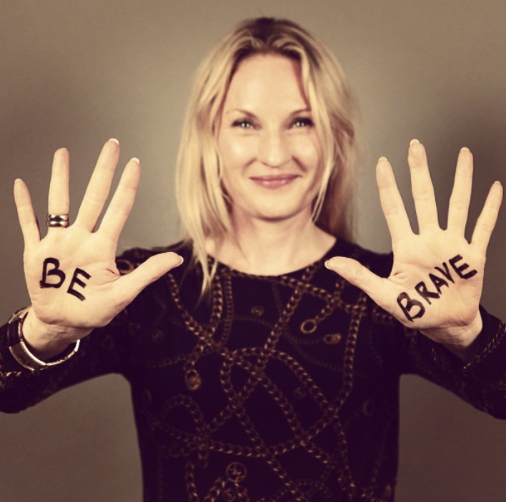 A woman smiling with the words 'BE' and 'BRAVE' written on her palms, showcasing a positive message.